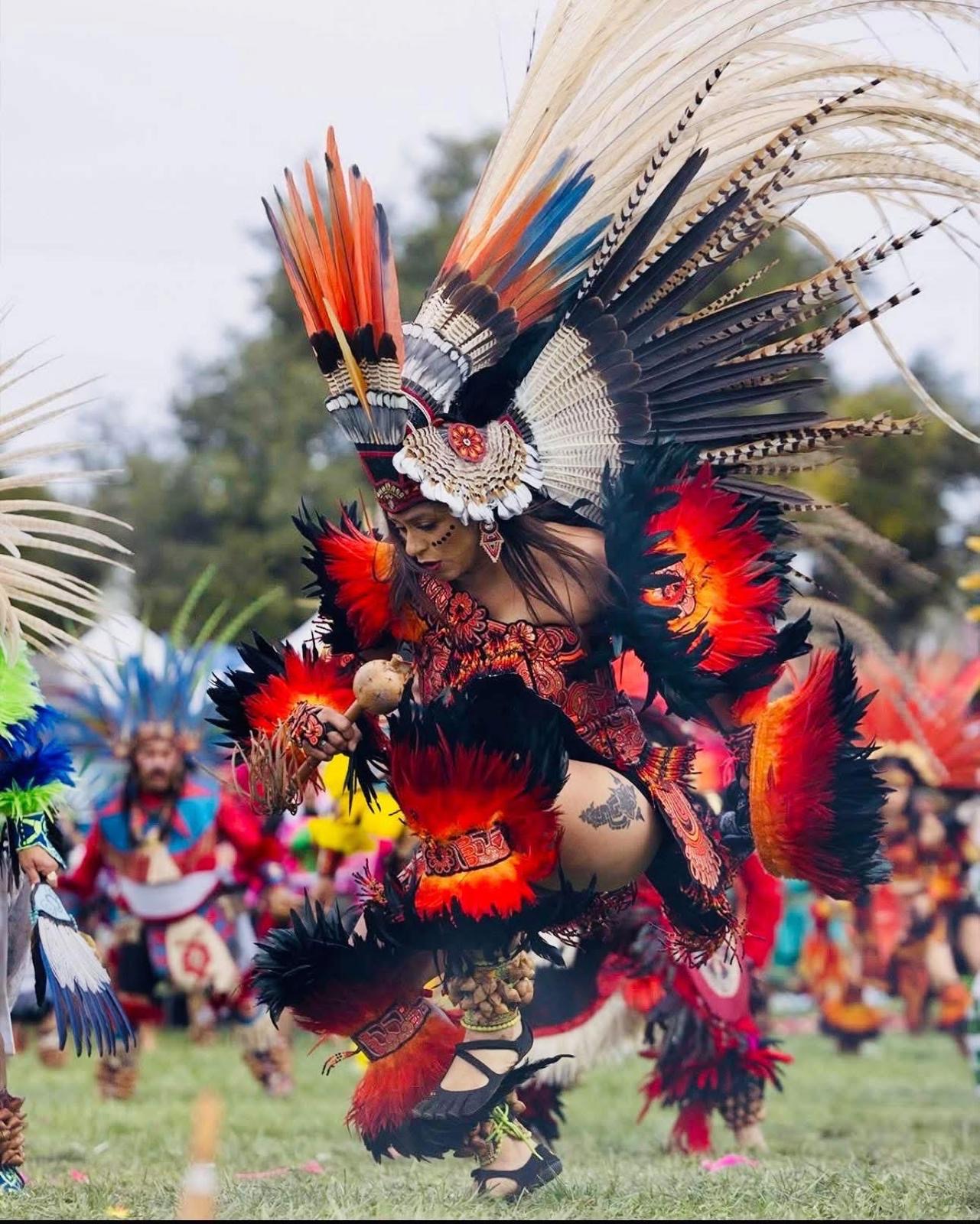 Aztec dancer in red and black feathered costume with maracas