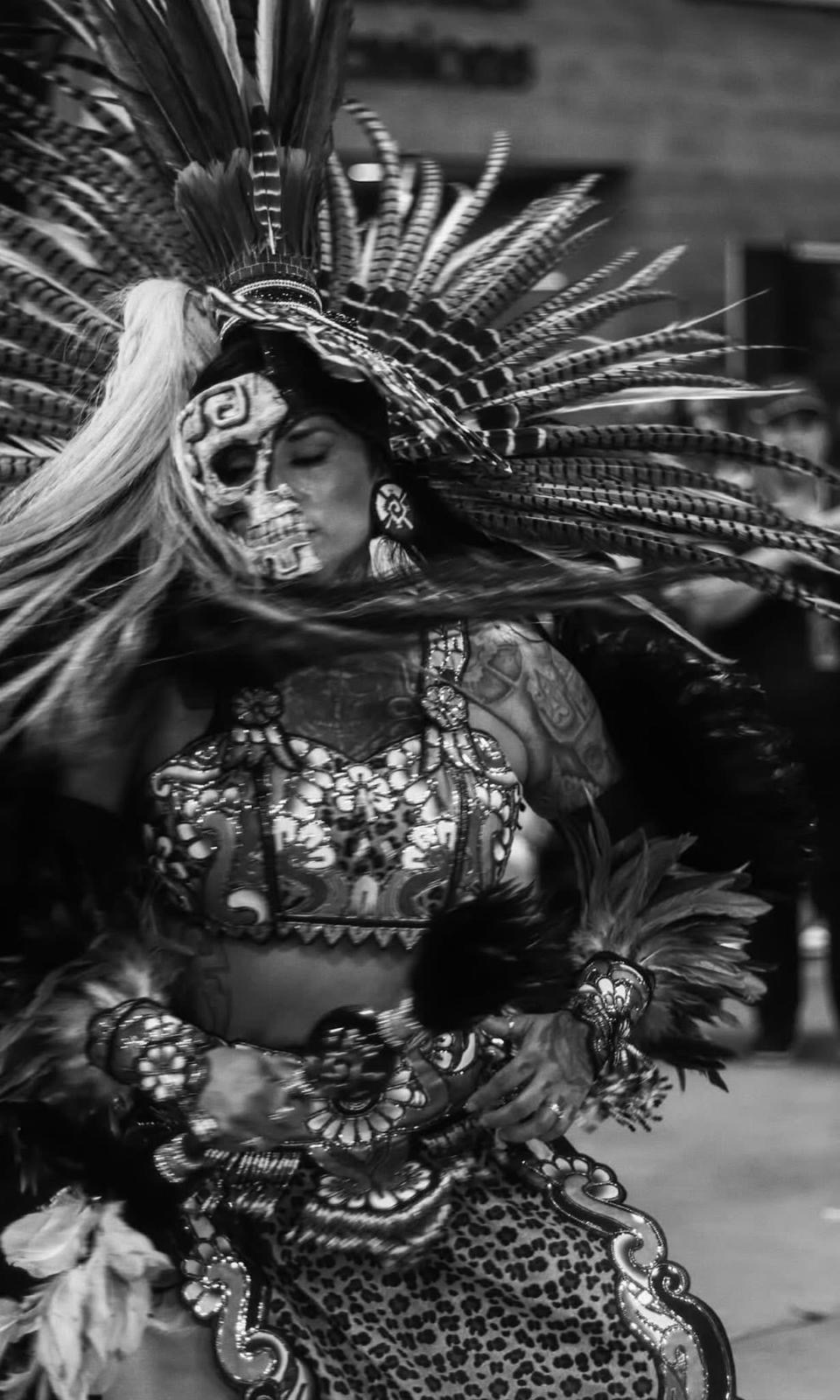 Black and white photo of dancer with skull face paint and feathered headdress