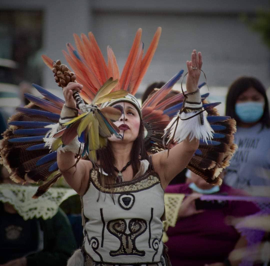 Female Aztec dancer with feathered headdress arms raised in prayer