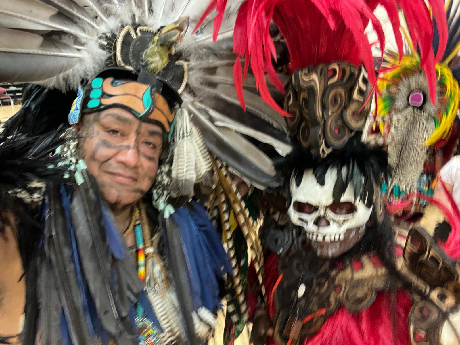 Two Aztec dancers in feathered regalia with skull mask