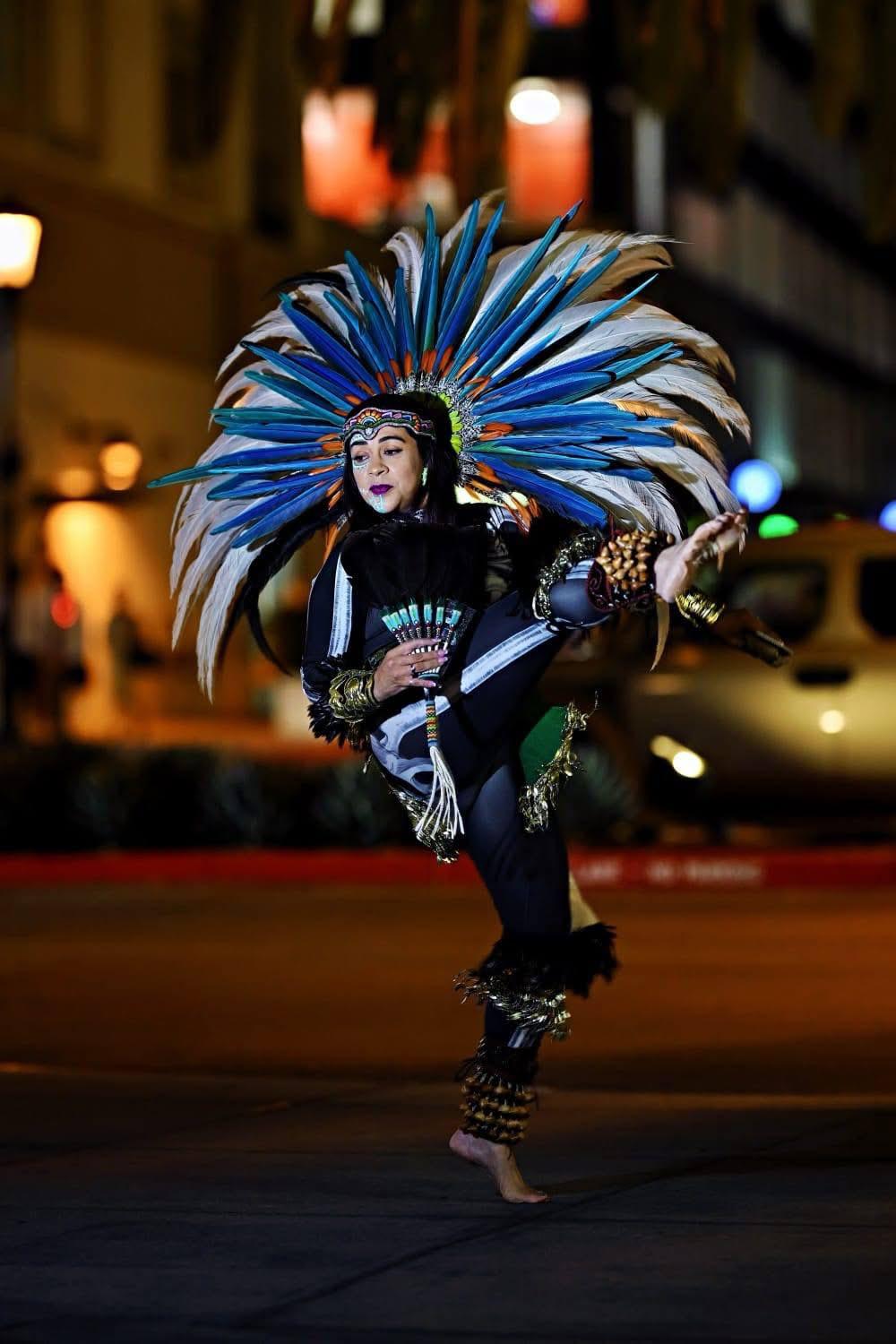 Female Aztec dancer in black outfit with blue and white feathered headdress leaping at night