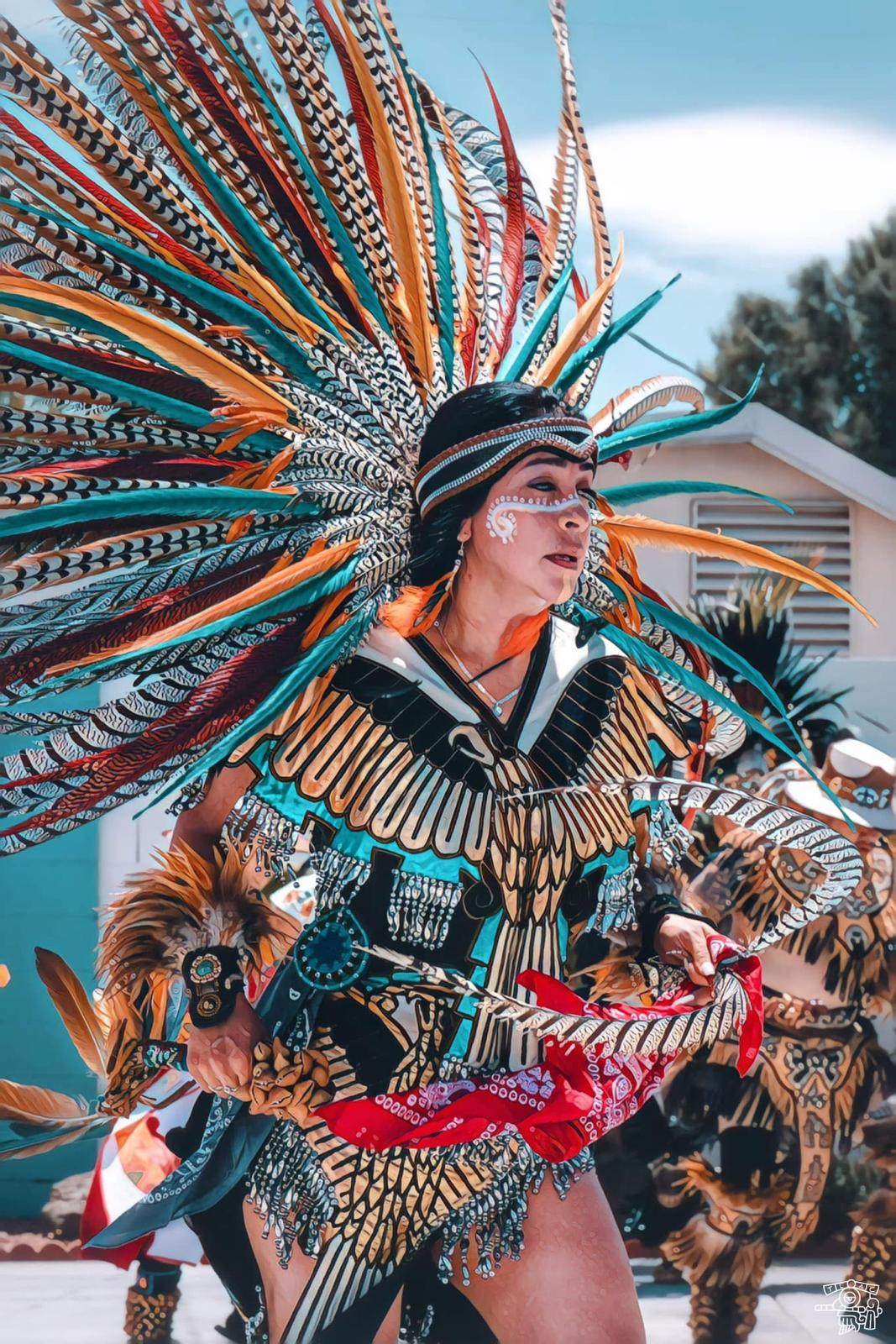 Female Aztec dancer in teal eagle regalia with large feathered headdress performing outdoors