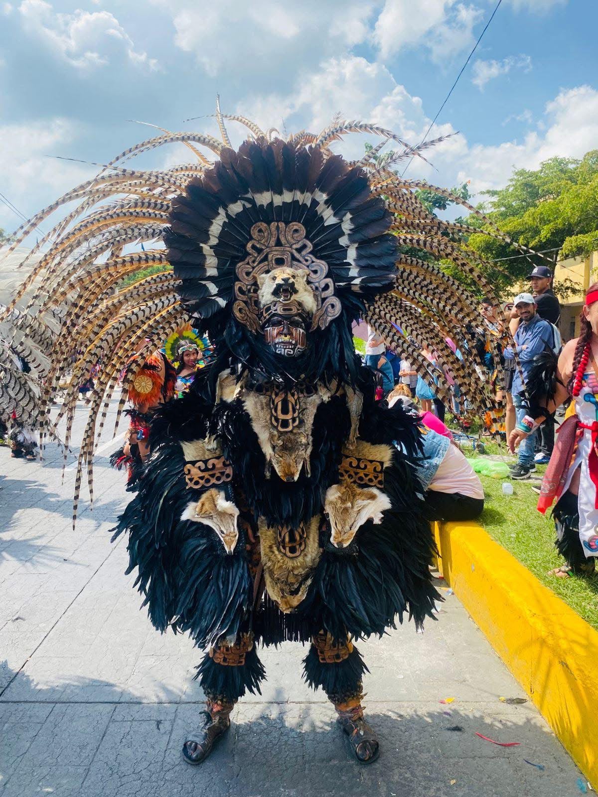 Aztec warrior in full black feathered headdress with bear skull mask standing tall